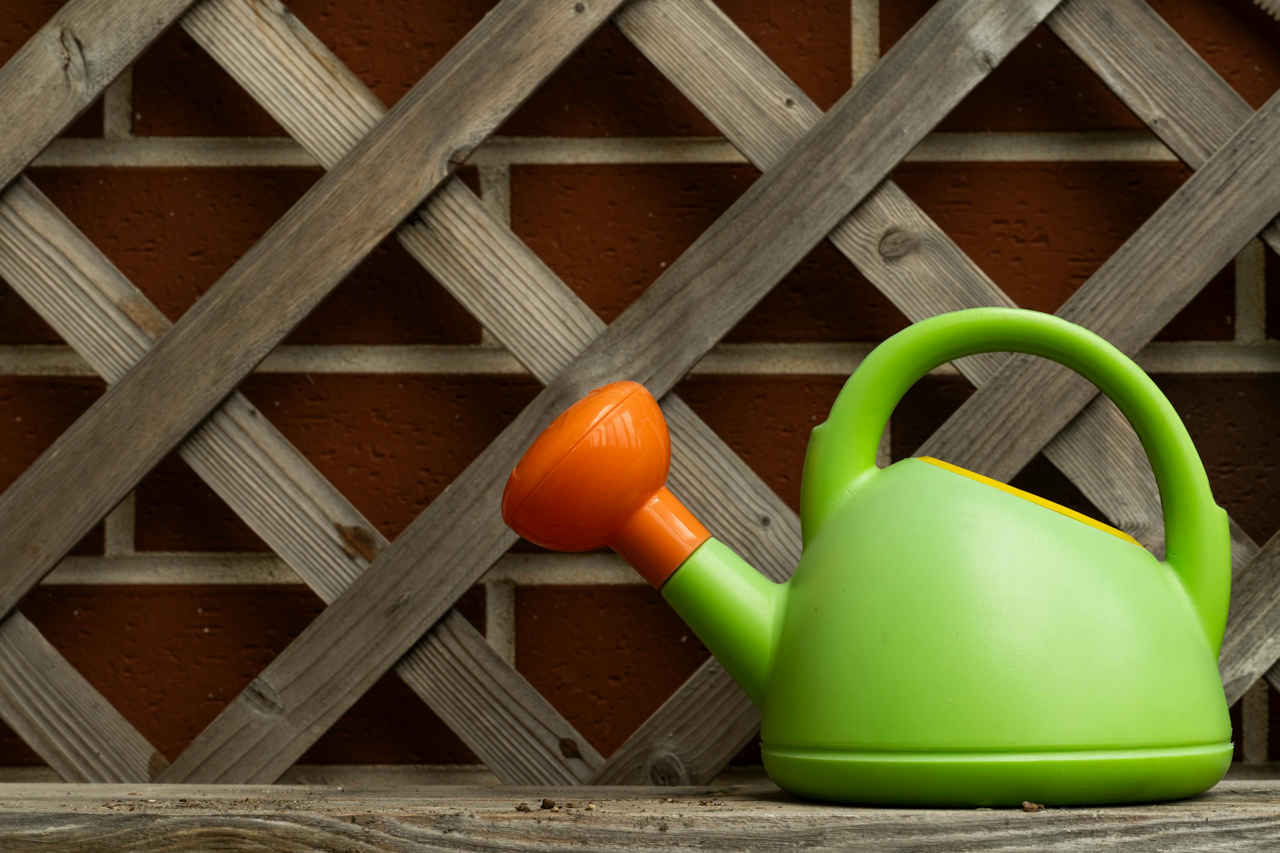 Bright green and orange watering can on a rustic wooden background, perfect for gardening themes.